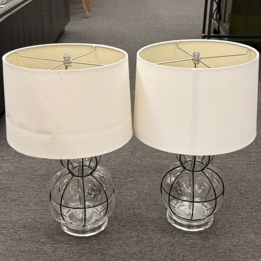 Two table lamps with glass bases and white lampshades on a gray floor.