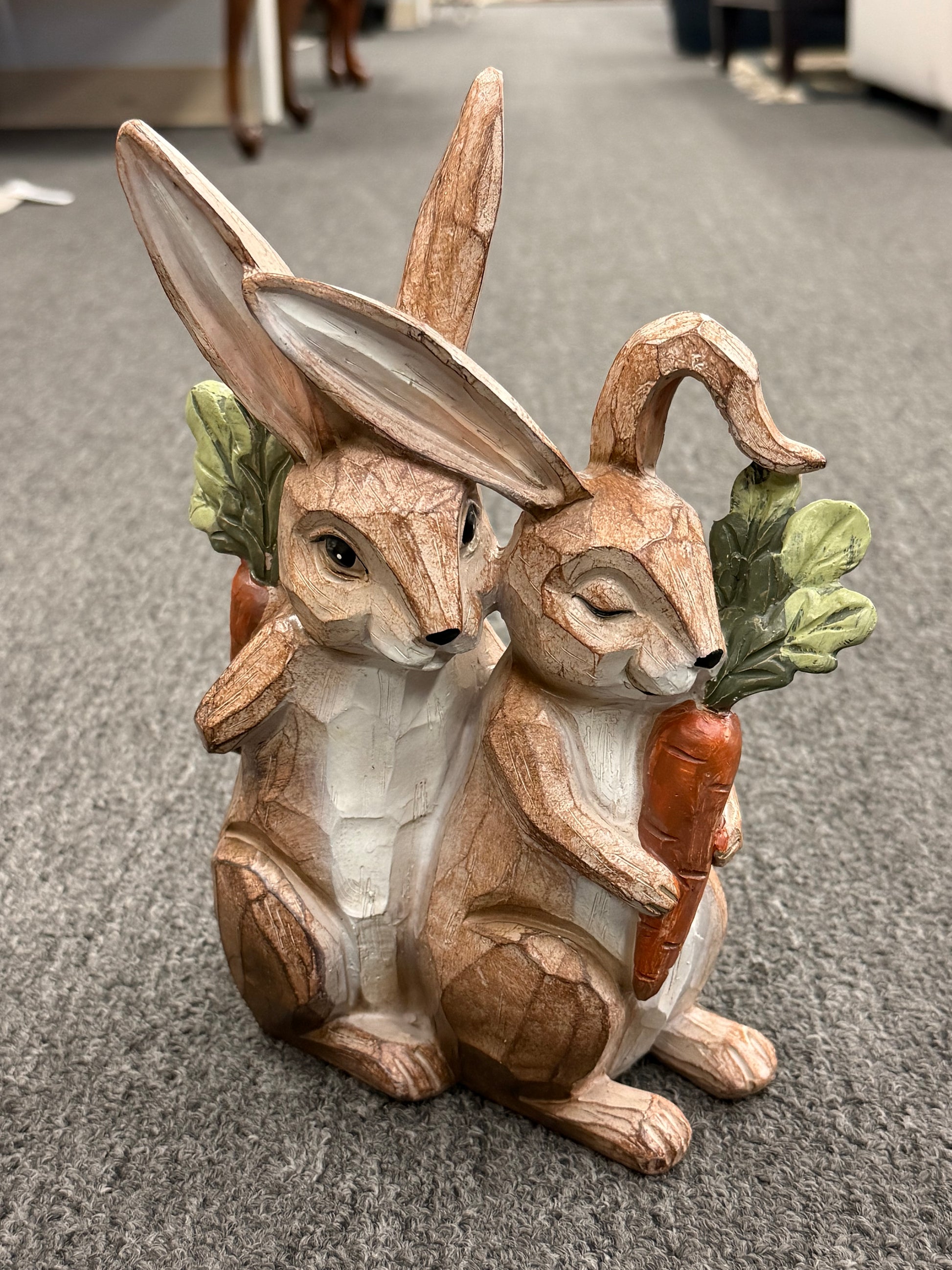 Wooden rabbit figurine holding a carrot on a gray carpeted floor