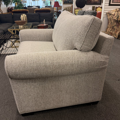 Gray upholstered armchair in a showroom setting with other furniture.