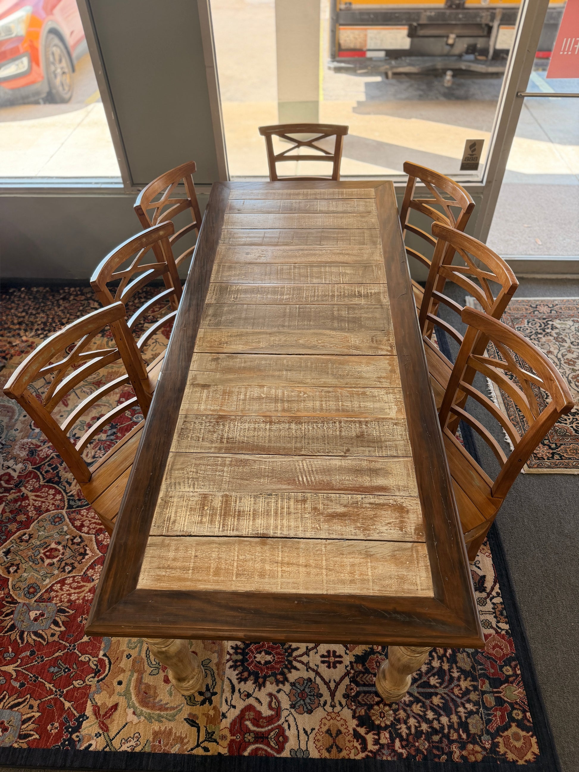 Long wooden dining table with chairs in a room with large windows.