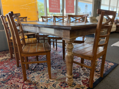 Wooden dining table with chairs on a patterned rug in a room with large windows.