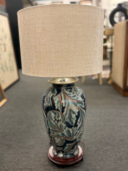 Decorative lamp with a patterned base and beige lampshade on a gray floor.