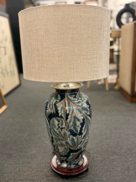 Decorative lamp with a patterned base and beige lampshade on a gray floor.