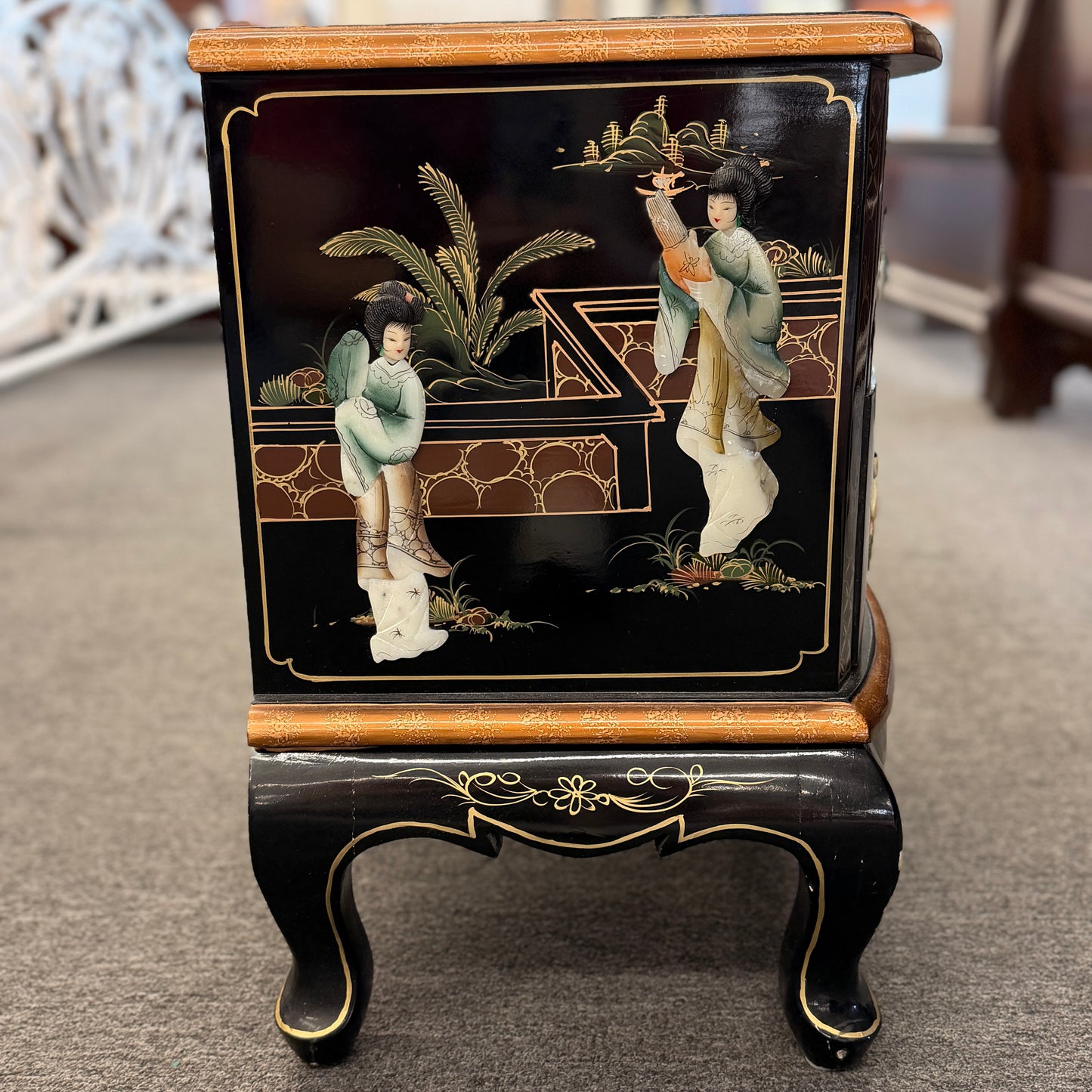 Decorative black cabinet with gold accents and figurines on a carpeted floor.