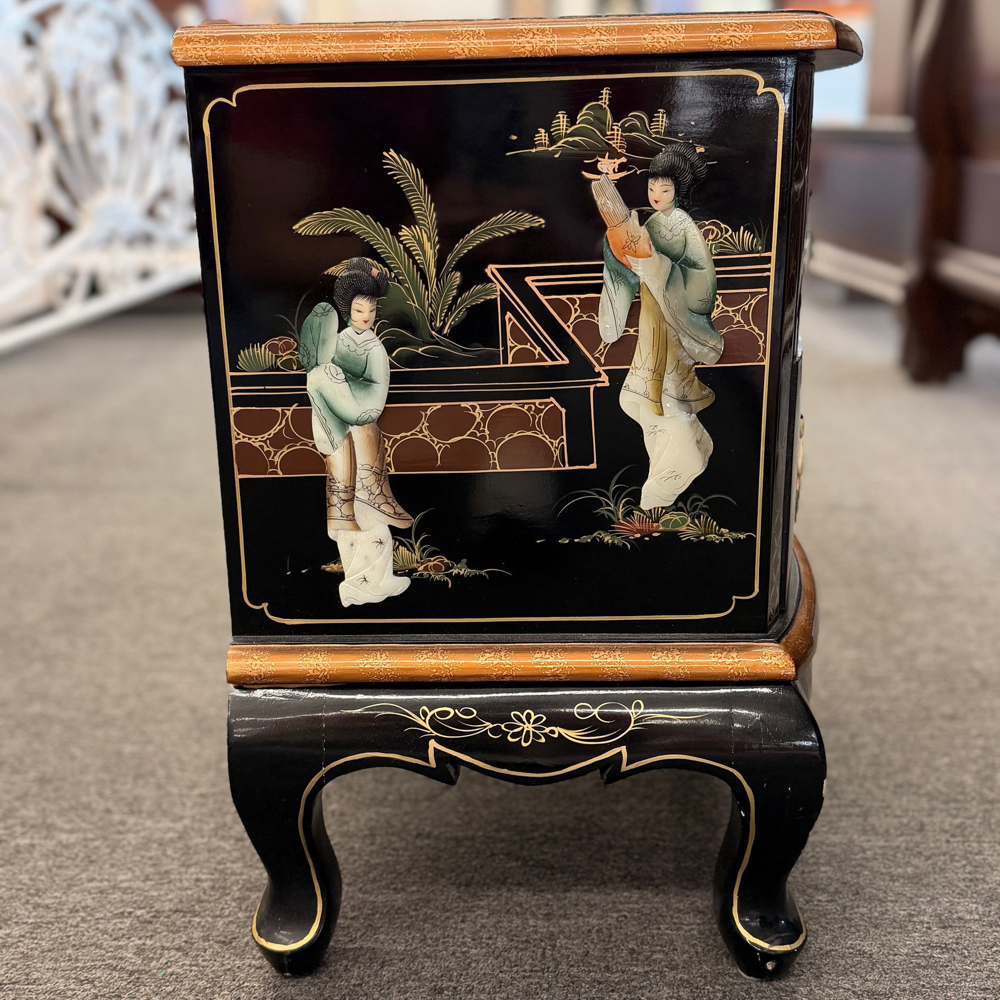 Decorative black cabinet with gold accents and figurines on a carpeted floor.