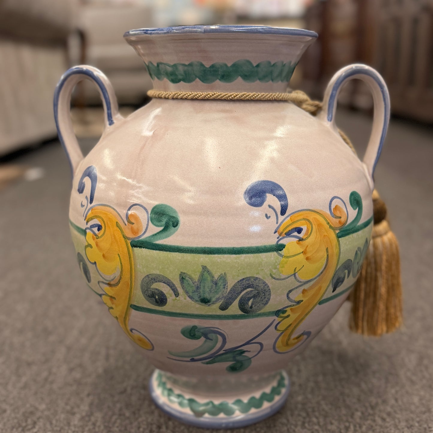 Tuscan farmhouse style ceramic floor and tabletop decorative vase featuring colorful patterns and a hanging tassel on a carpeted floor at 2nd Debut Houston consignment showroom