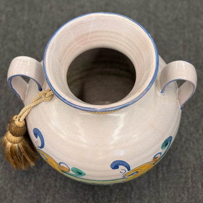Decorative ceramic vase with handles and a tassel on a dark background