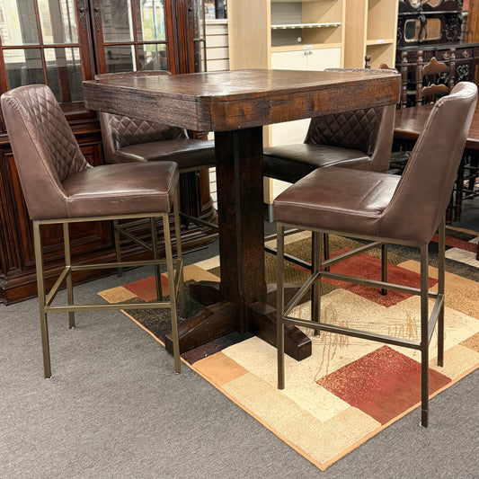 Wooden bar table with four brown leather stools in a room setting.