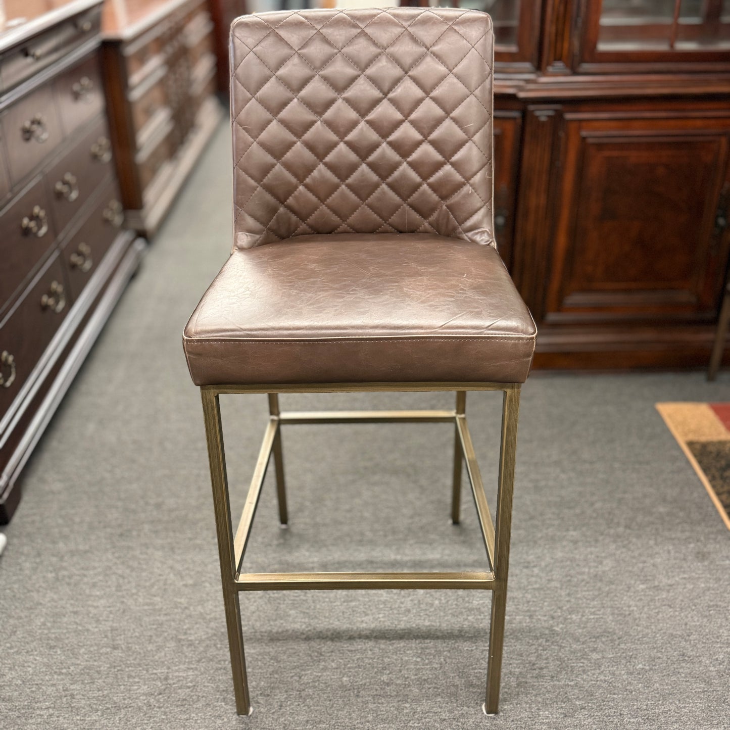 Brown bar stool with quilted backrest in a room with wooden furniture.