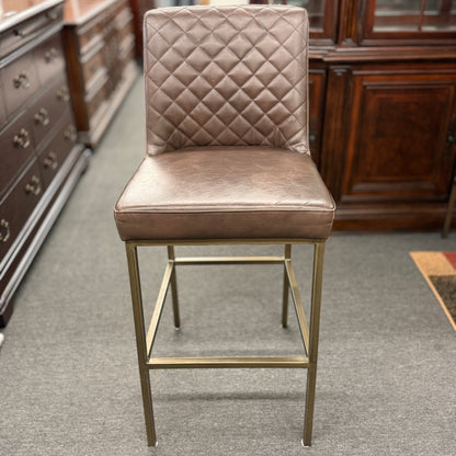 Brown bar stool with quilted backrest in a room with wooden furniture.