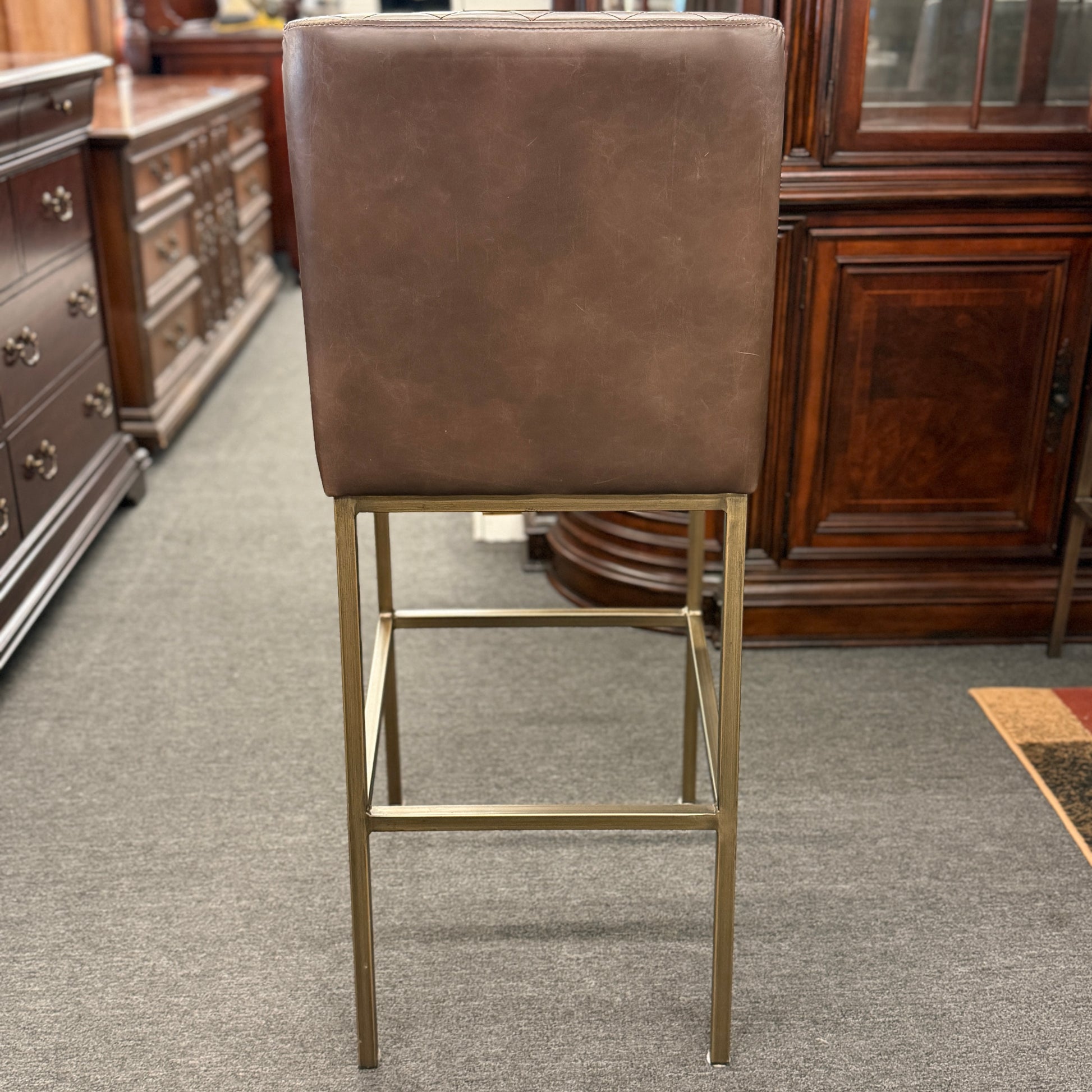 Brown bar stool with metal legs in a room with wooden furniture.