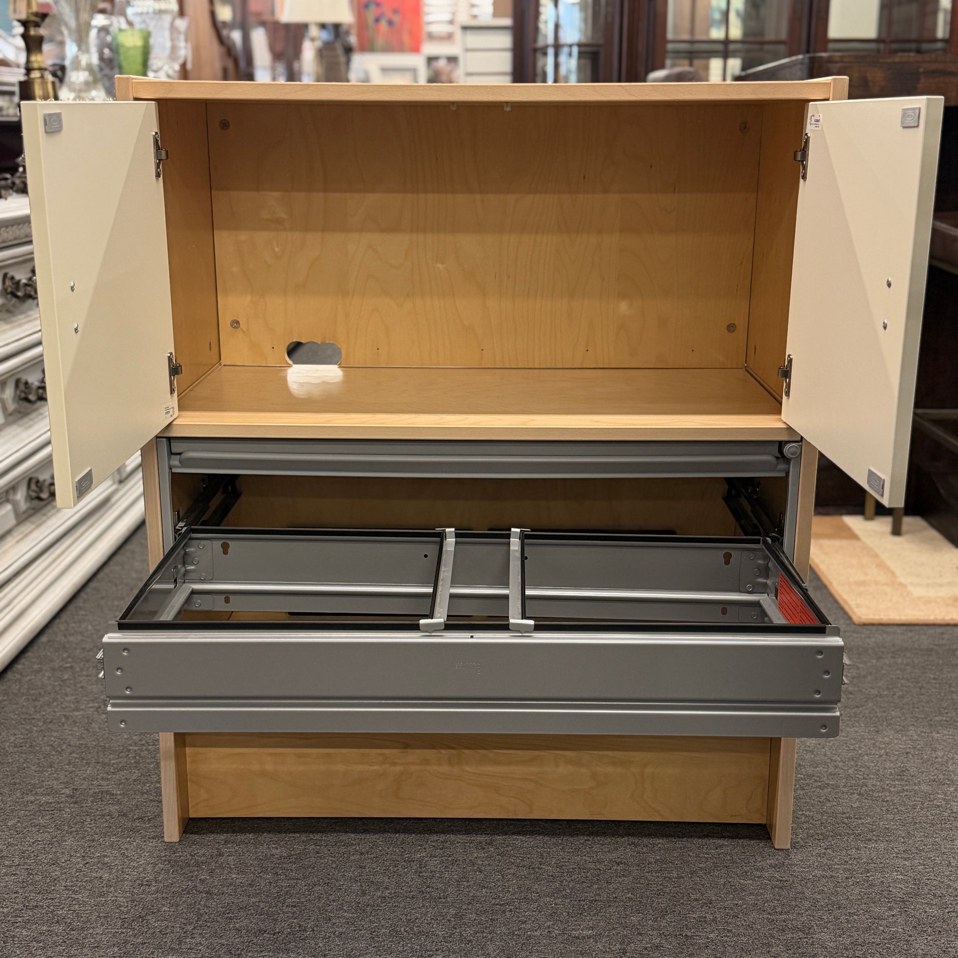 Wooden storage unit with open doors and drawers on a carpeted floor.
