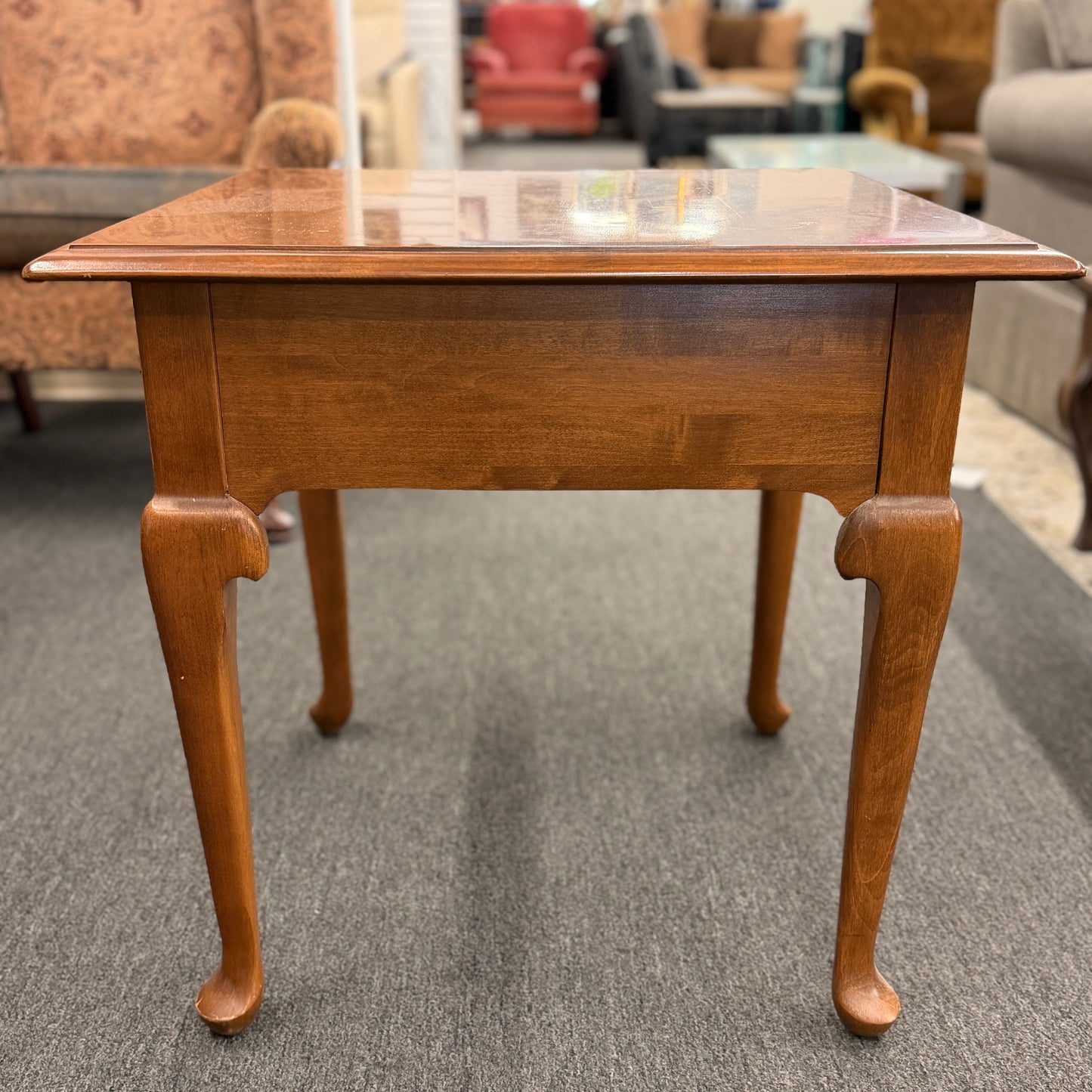 Wooden side table on a carpeted floor with furniture in the background