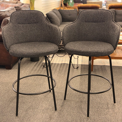 Two gray bar stools with black metal legs in a room setting.