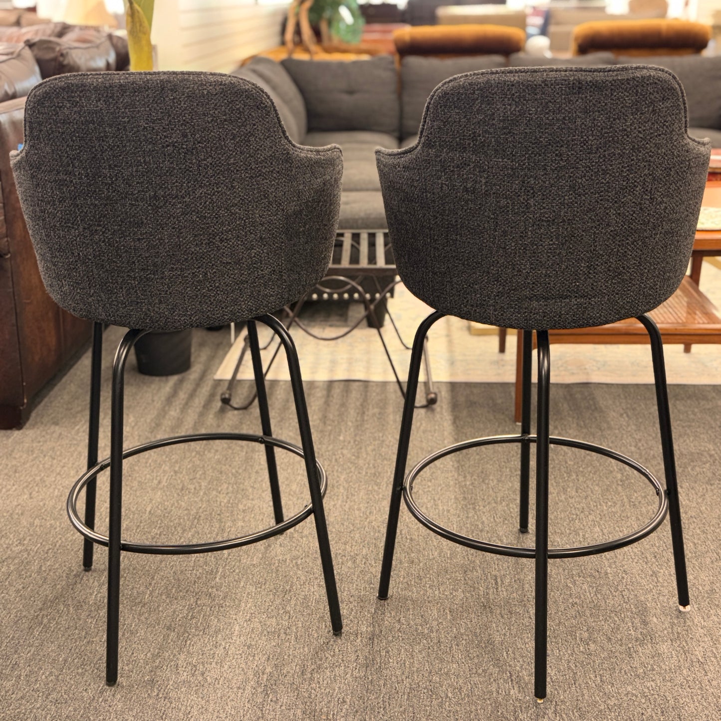Two gray bar stools with black metal legs in a room with furniture.