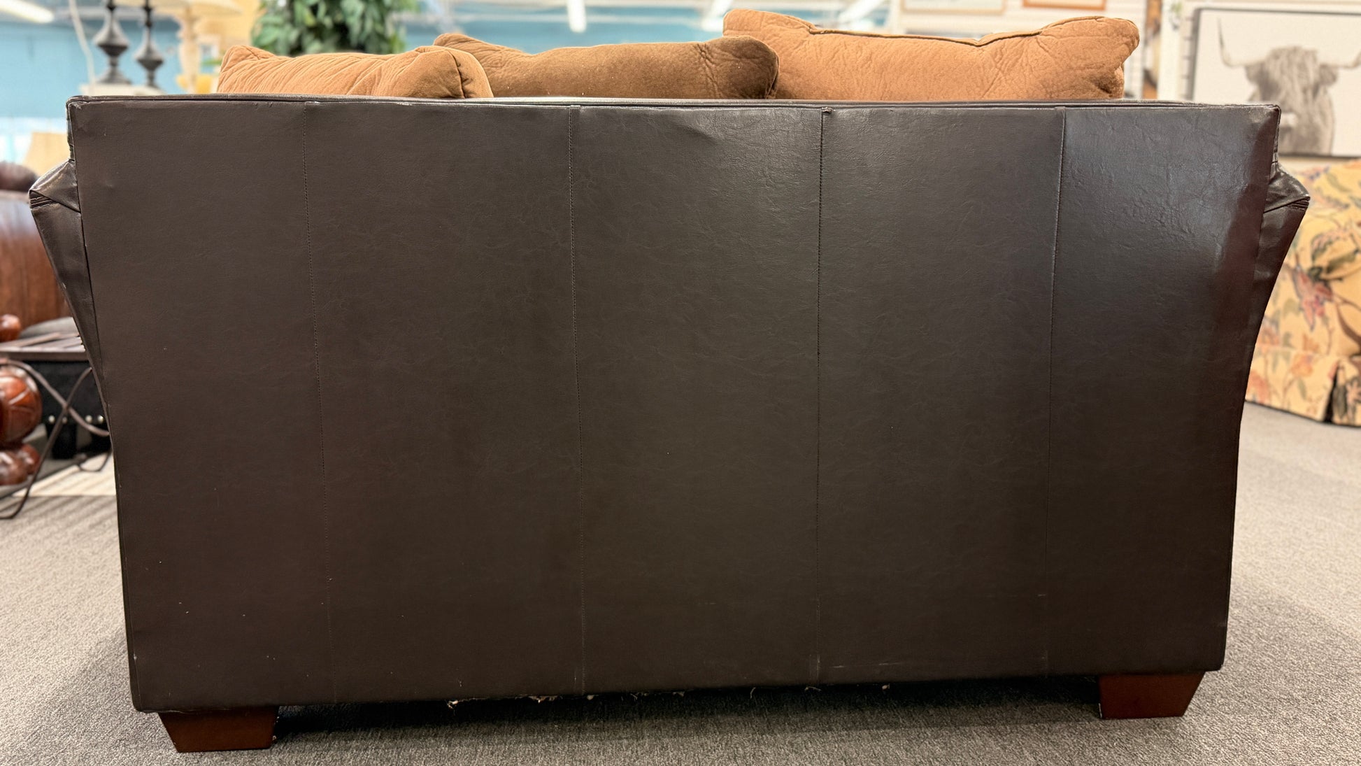 Brown leather sofa with wooden legs on a gray floor.
