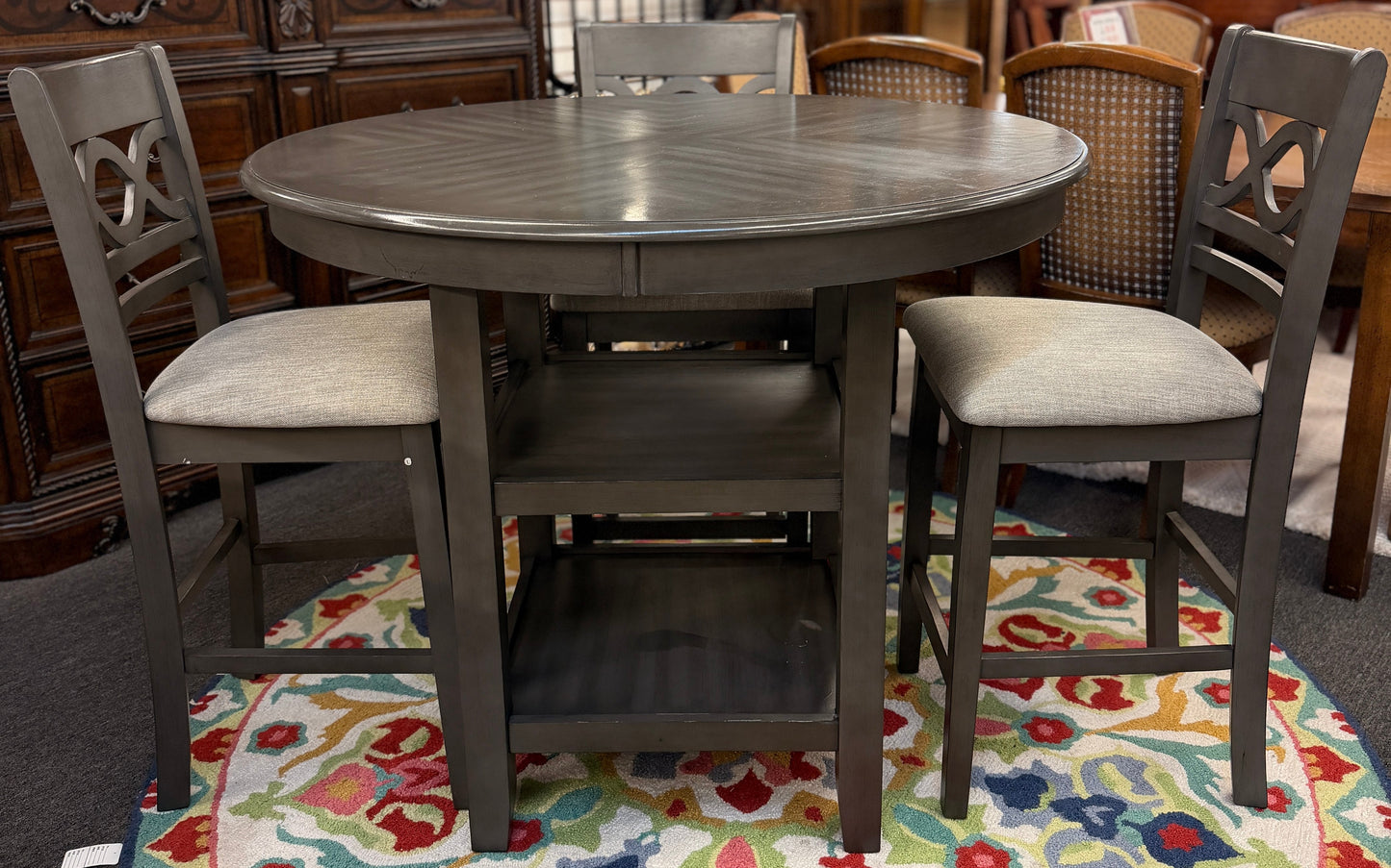 Round wooden dining table with four chairs on a patterned rug in a furniture store.
