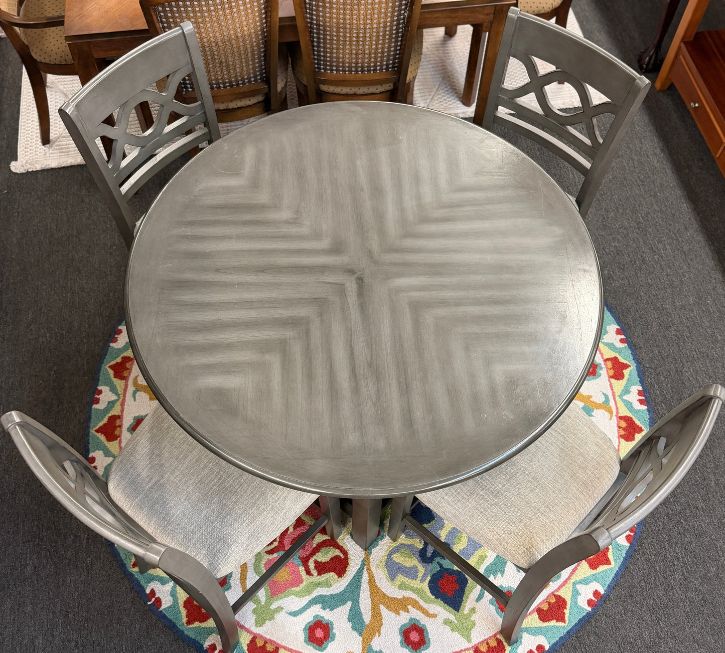 Round metal table with four matching chairs on a colorful rug in a room.