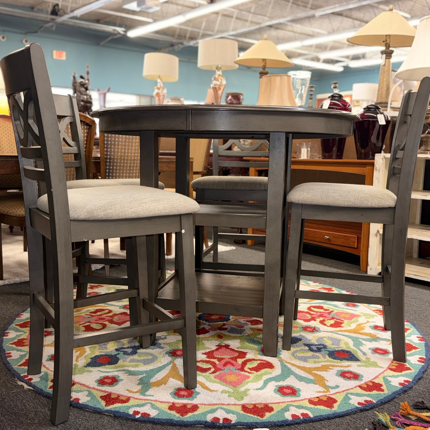 Round dining table with four chairs on a colorful rug in a furniture store.