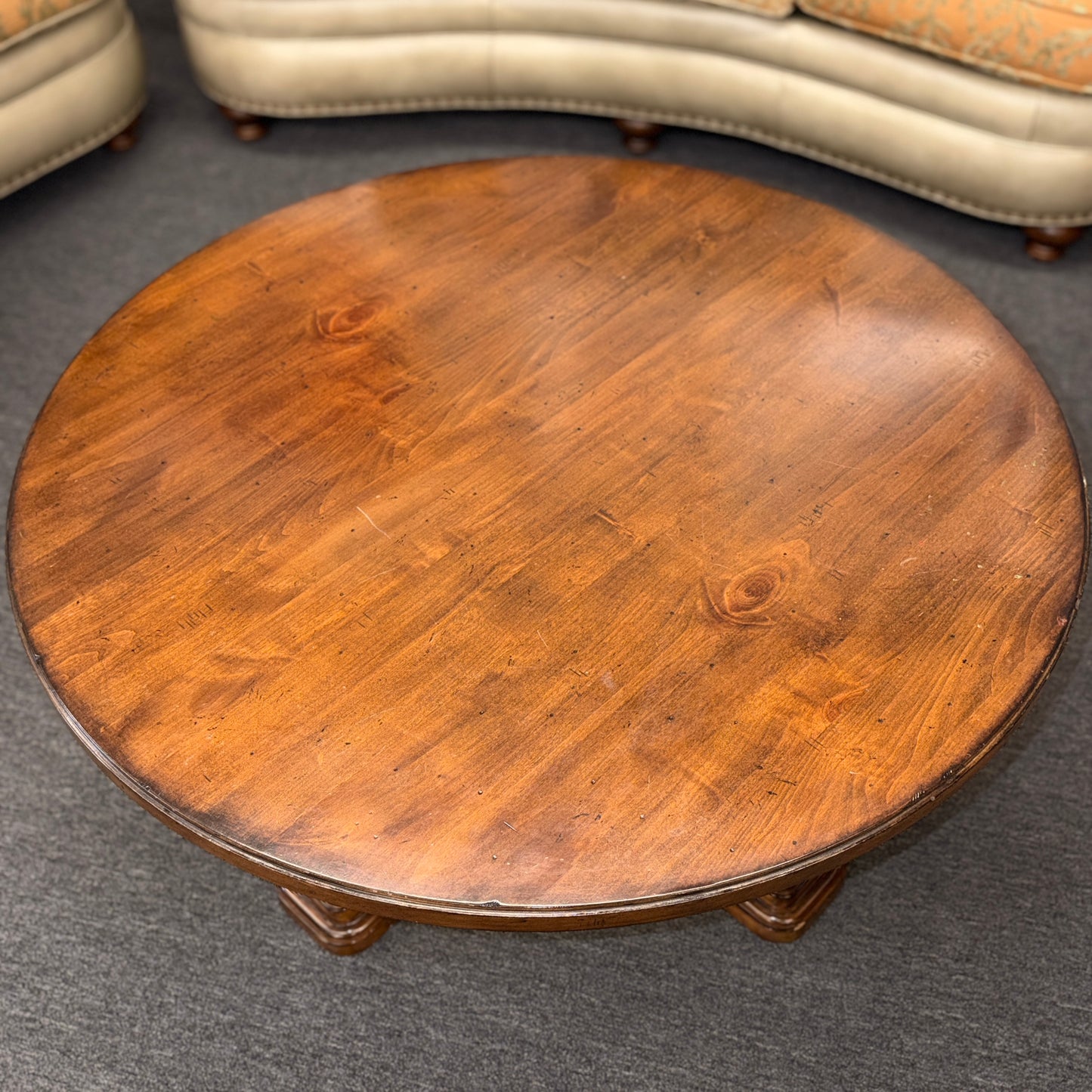 Round wooden table on a gray carpeted floor with a beige sofa in the background.