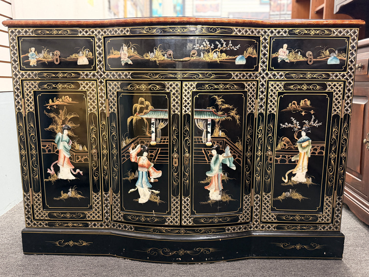 Decorative black cabinet with intricate gold and white designs featuring people and landscapes.