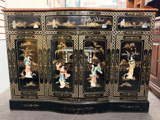 Decorative black cabinet with intricate gold and white designs featuring people and landscapes.