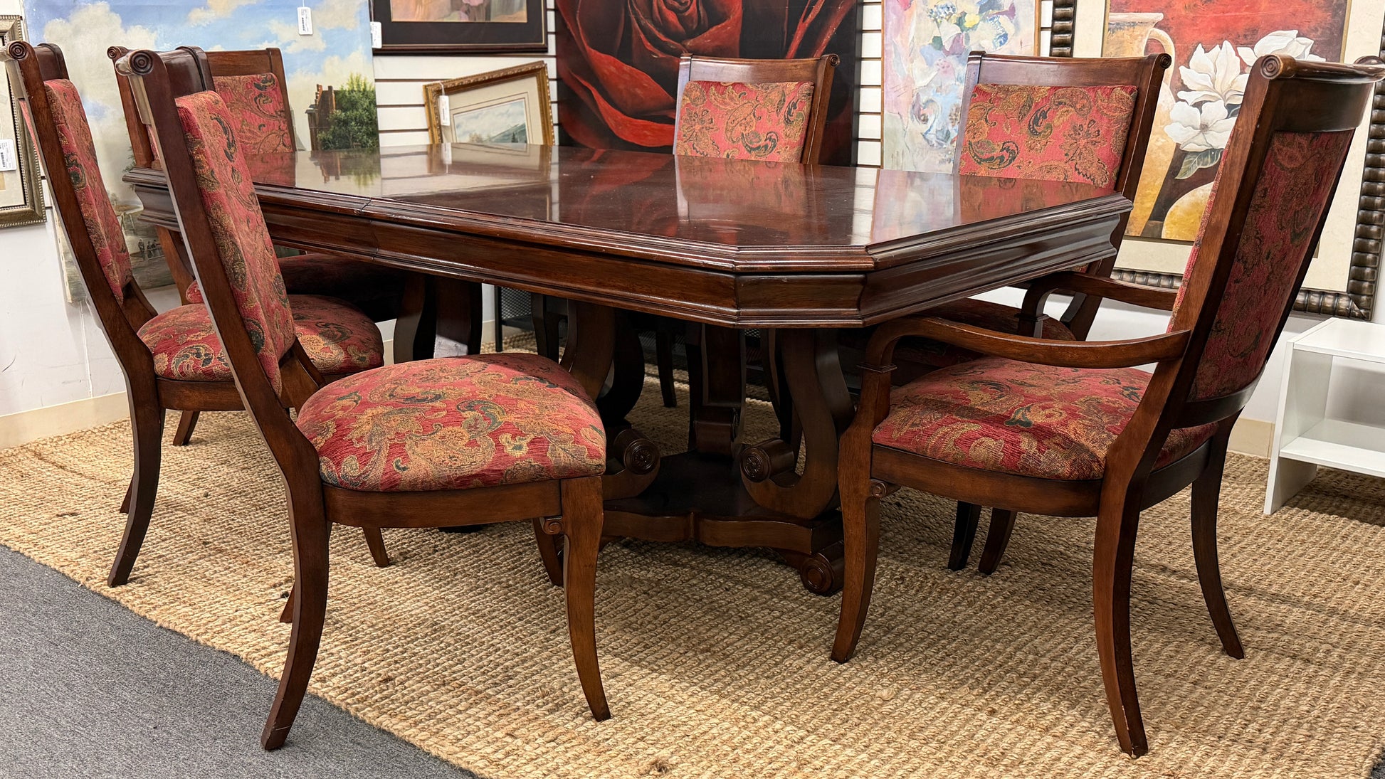 Wooden dining table with six matching chairs in a room with framed pictures on the wall.