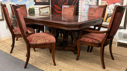 Wooden dining table with six matching chairs in a room with framed pictures on the wall.