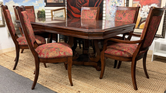 Wooden dining table with six matching chairs in a room with framed pictures on the wall.