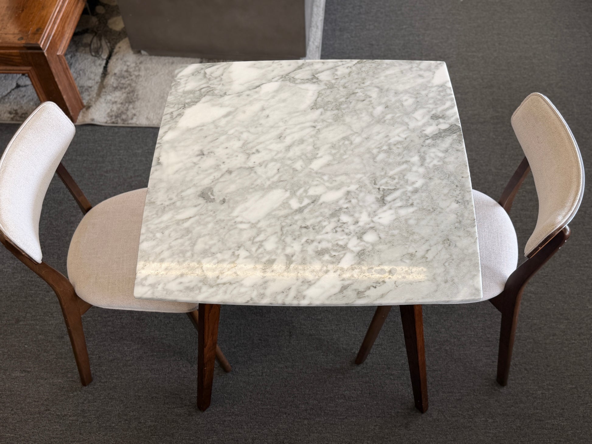 Square marble table with four chairs on a dark floor