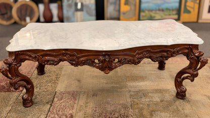 Decorative bench with marble top and ornate wooden legs on a textured floor.