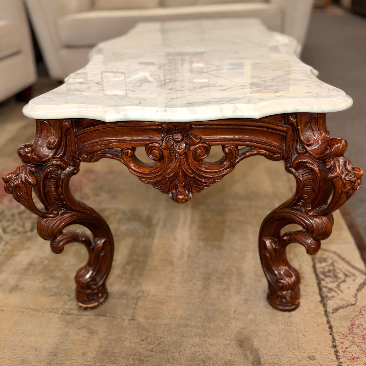 Decorative coffee table with marble top and wooden base on a carpeted floor.