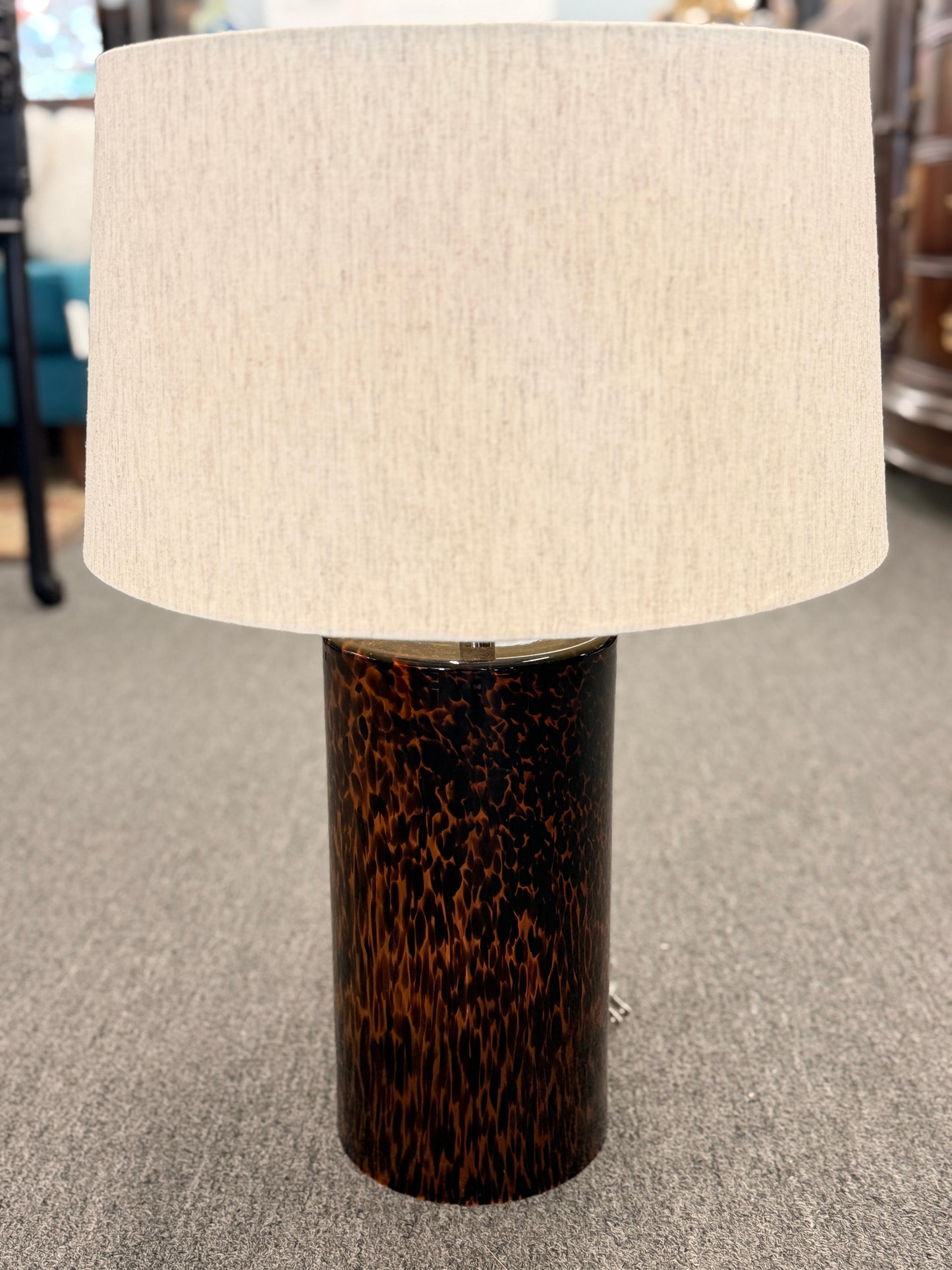 Table lamp with a tortoiseshell base and beige lampshade on a carpeted floor.