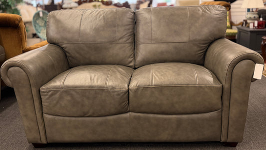 Gray leather sofa in a store setting with other furniture items.