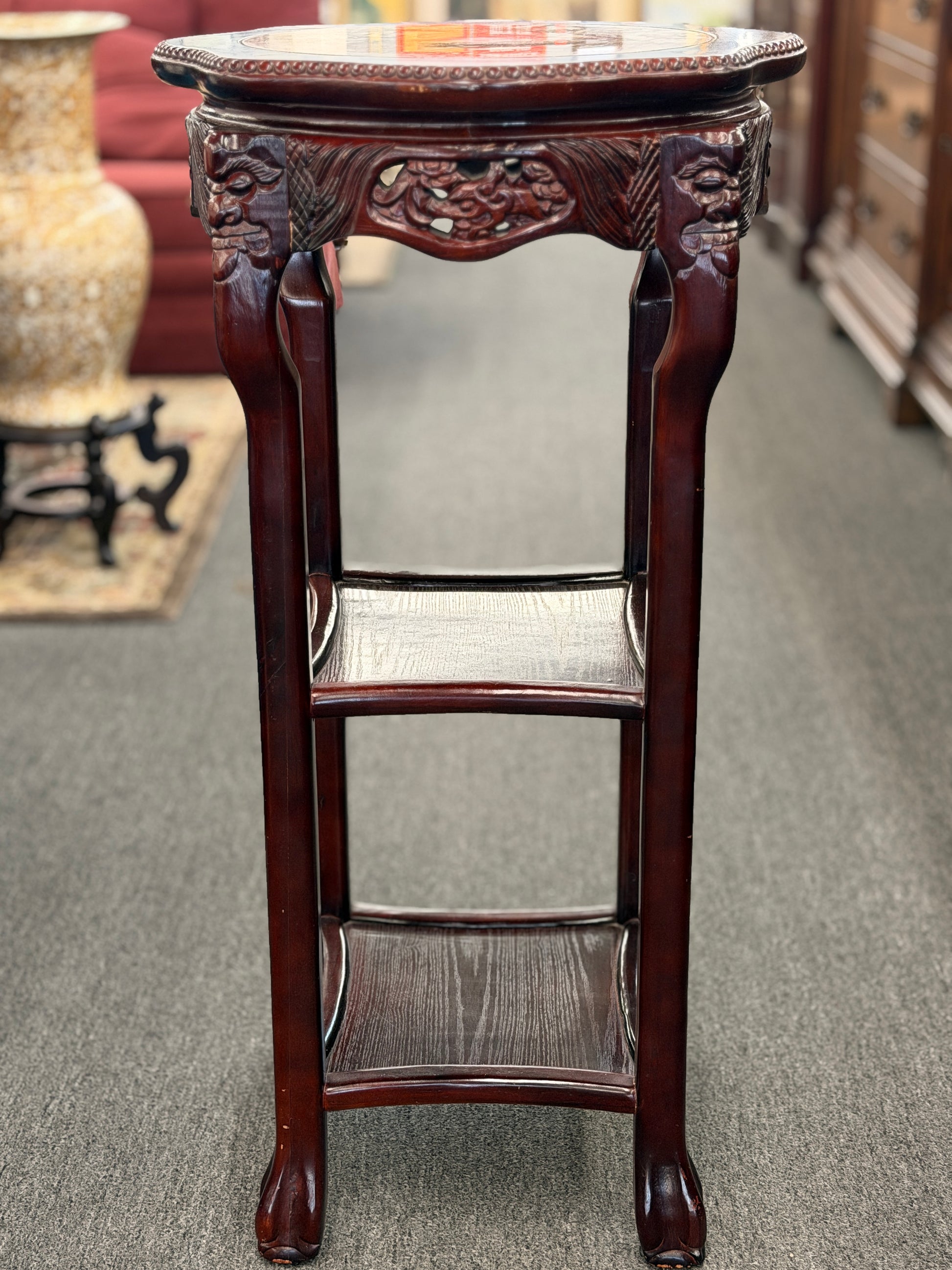 Decorative wooden plant stand with intricate carvings on a carpeted floor.