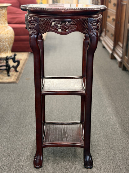 Decorative wooden pedestal table with intricate carvings on a carpeted floor.