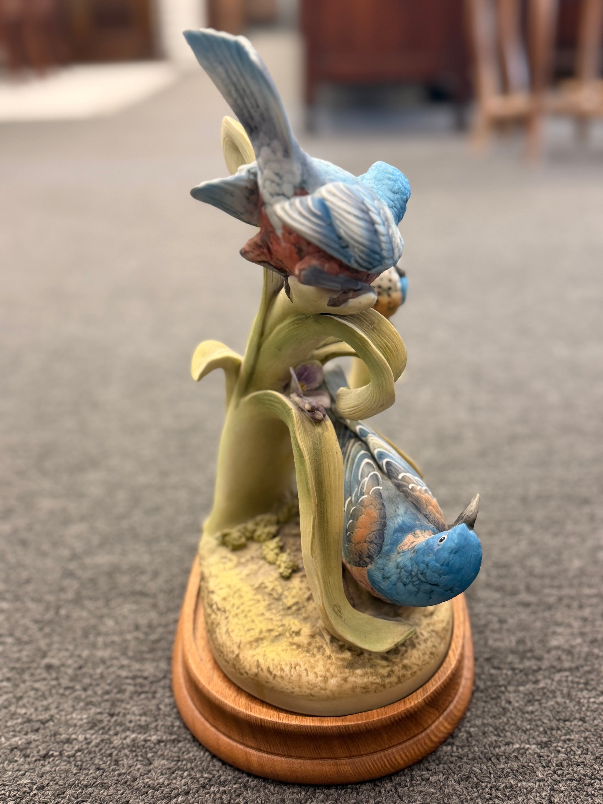 Decorative figurine of birds on a branch with a wooden base on a carpeted floor.