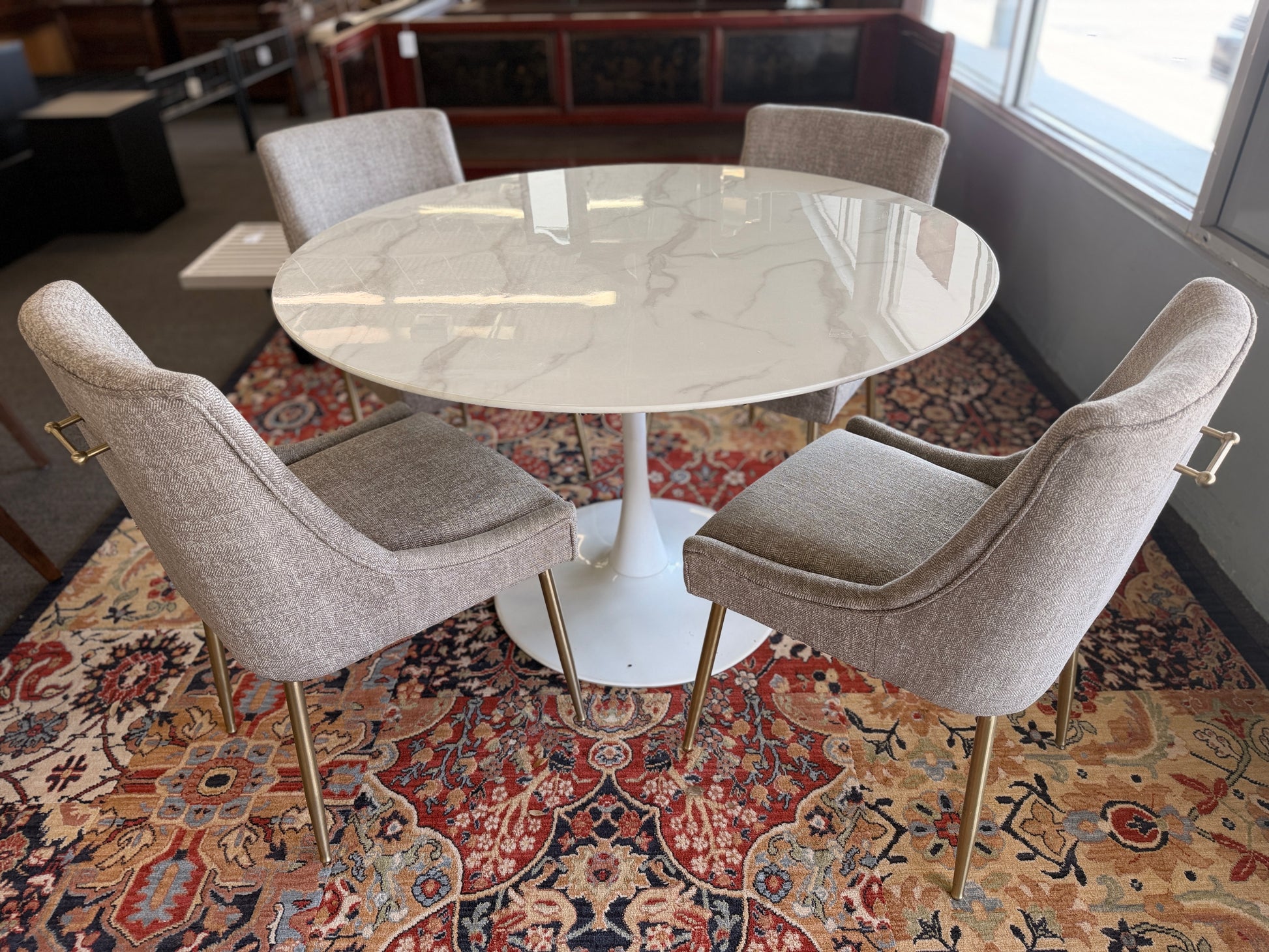 Round marble table with four chairs on a patterned rug in a room.