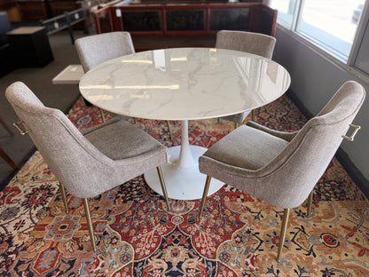 Round marble table with four chairs on a patterned rug in a room.