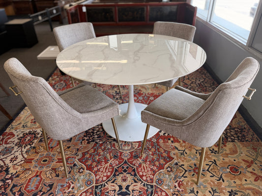 Round marble table with four chairs on a patterned rug in a room.