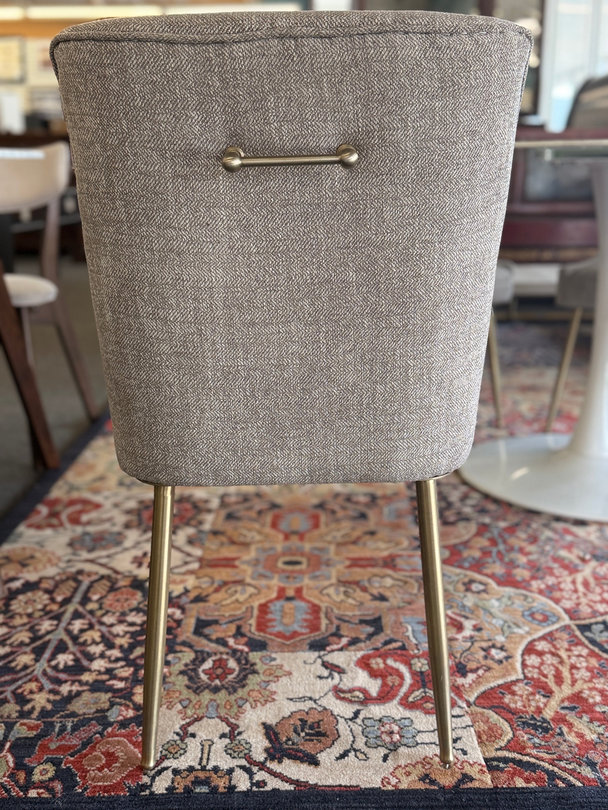 Gray upholstered chair with gold legs on a patterned rug