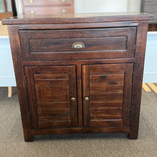 Wooden cabinet with two doors and a drawer on a carpeted floor.