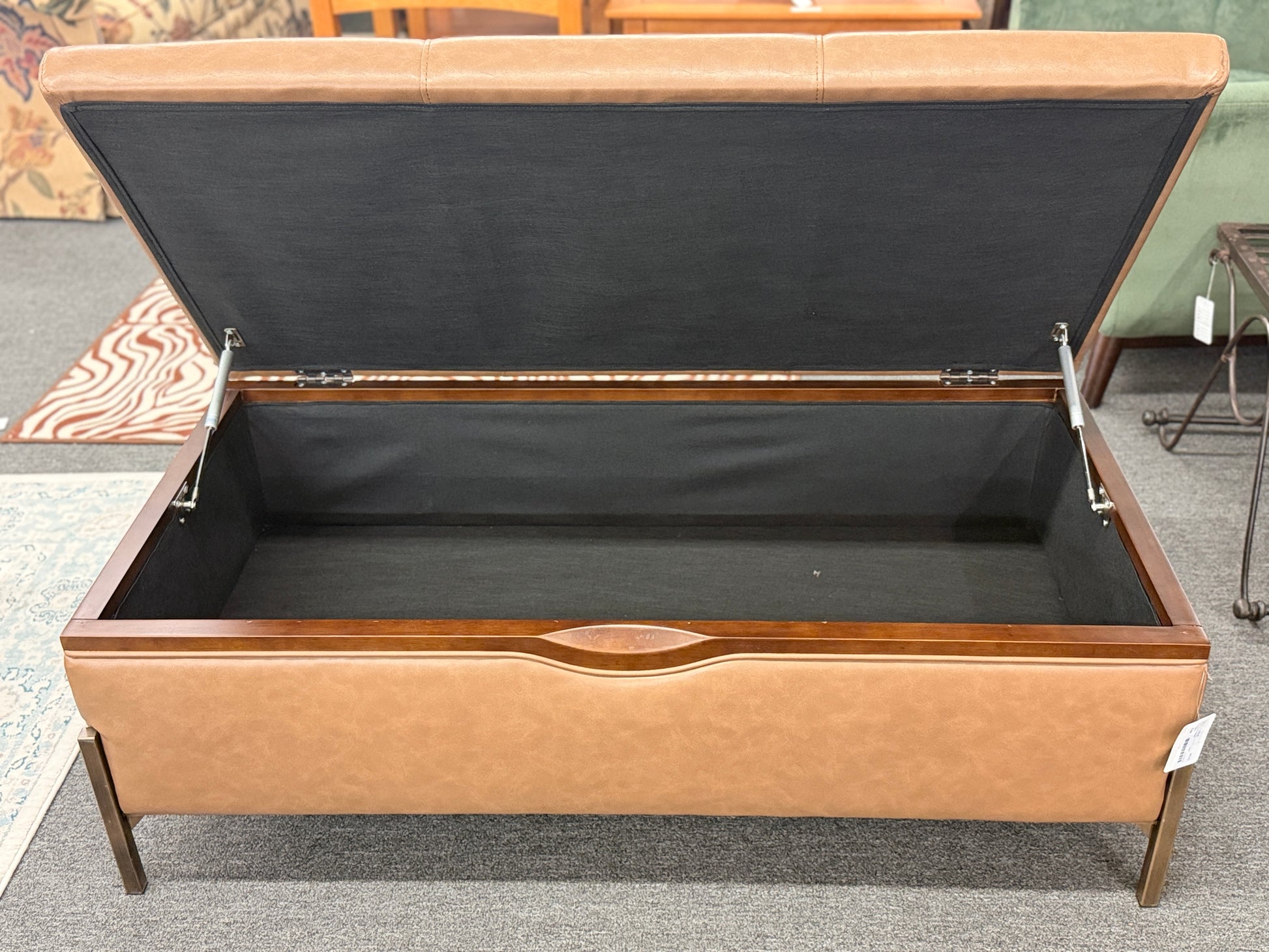 Brown leather storage bench with open lid on a carpeted floor