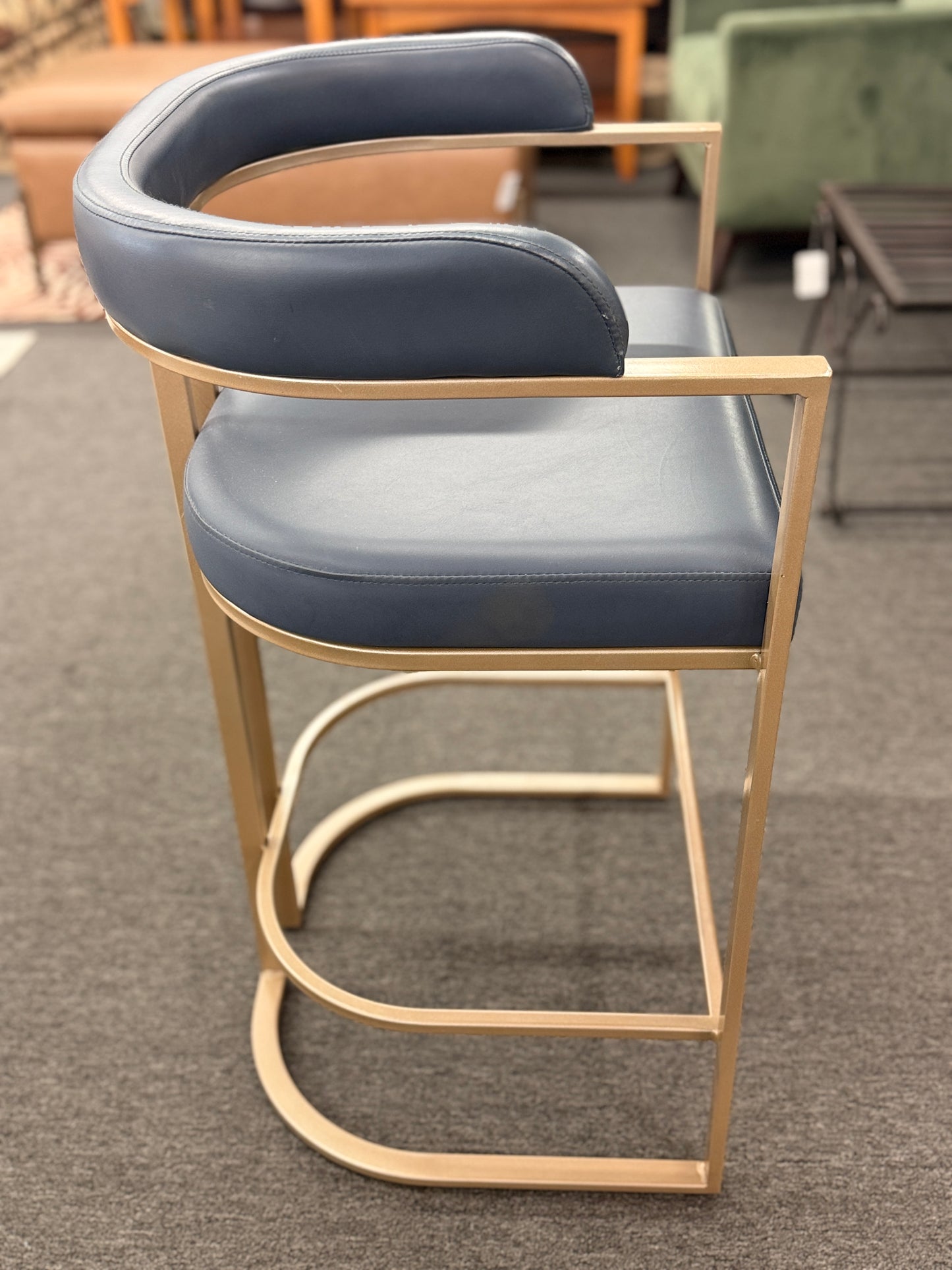 Modern bar stool with blue cushioned seat and gold frame on a gray floor.