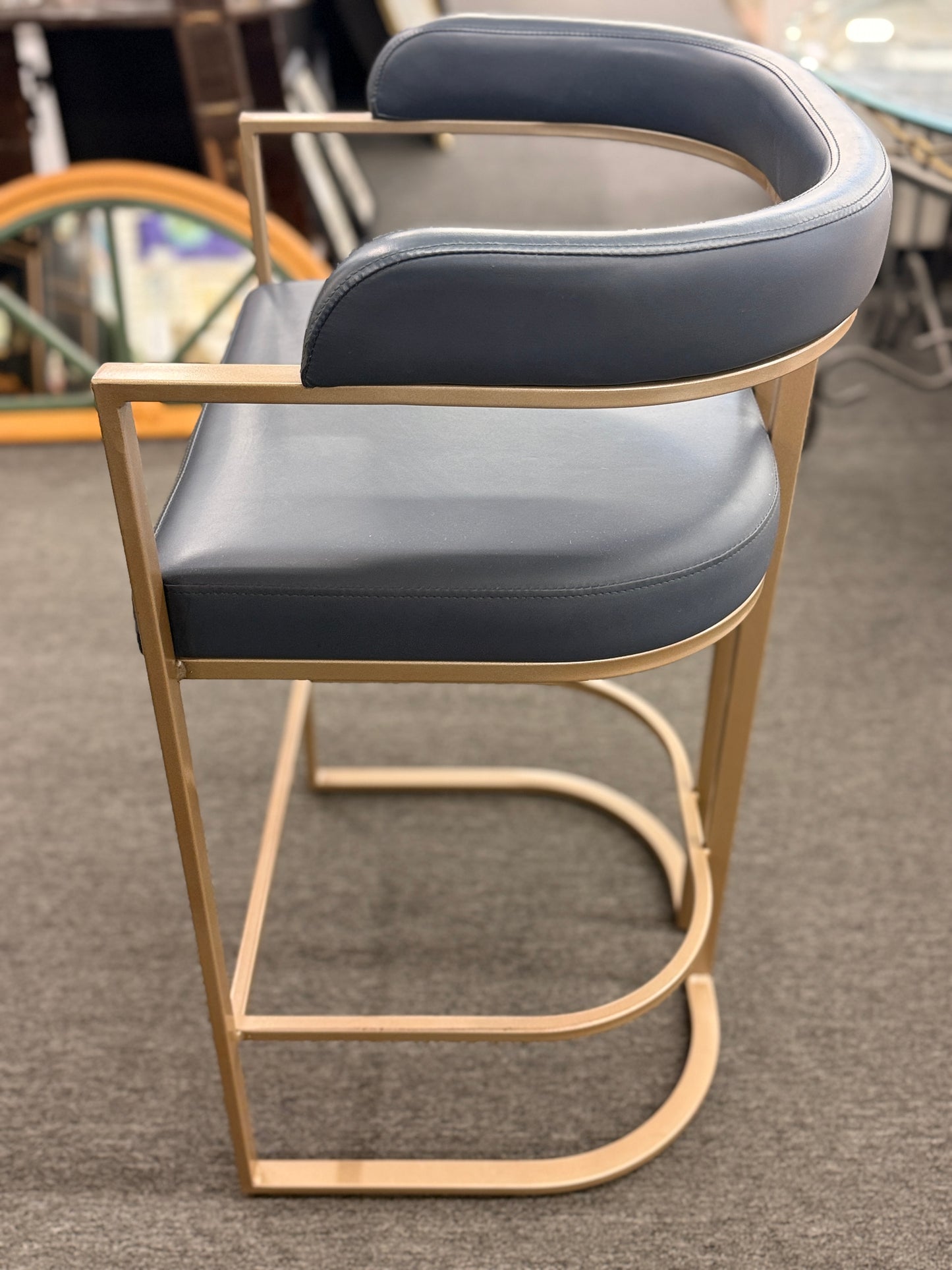 Bar stool with blue cushioned seat and gold frame on a gray floor.