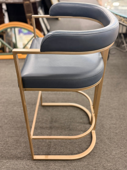 Bar stool with blue cushioned seat and gold frame on a gray floor.