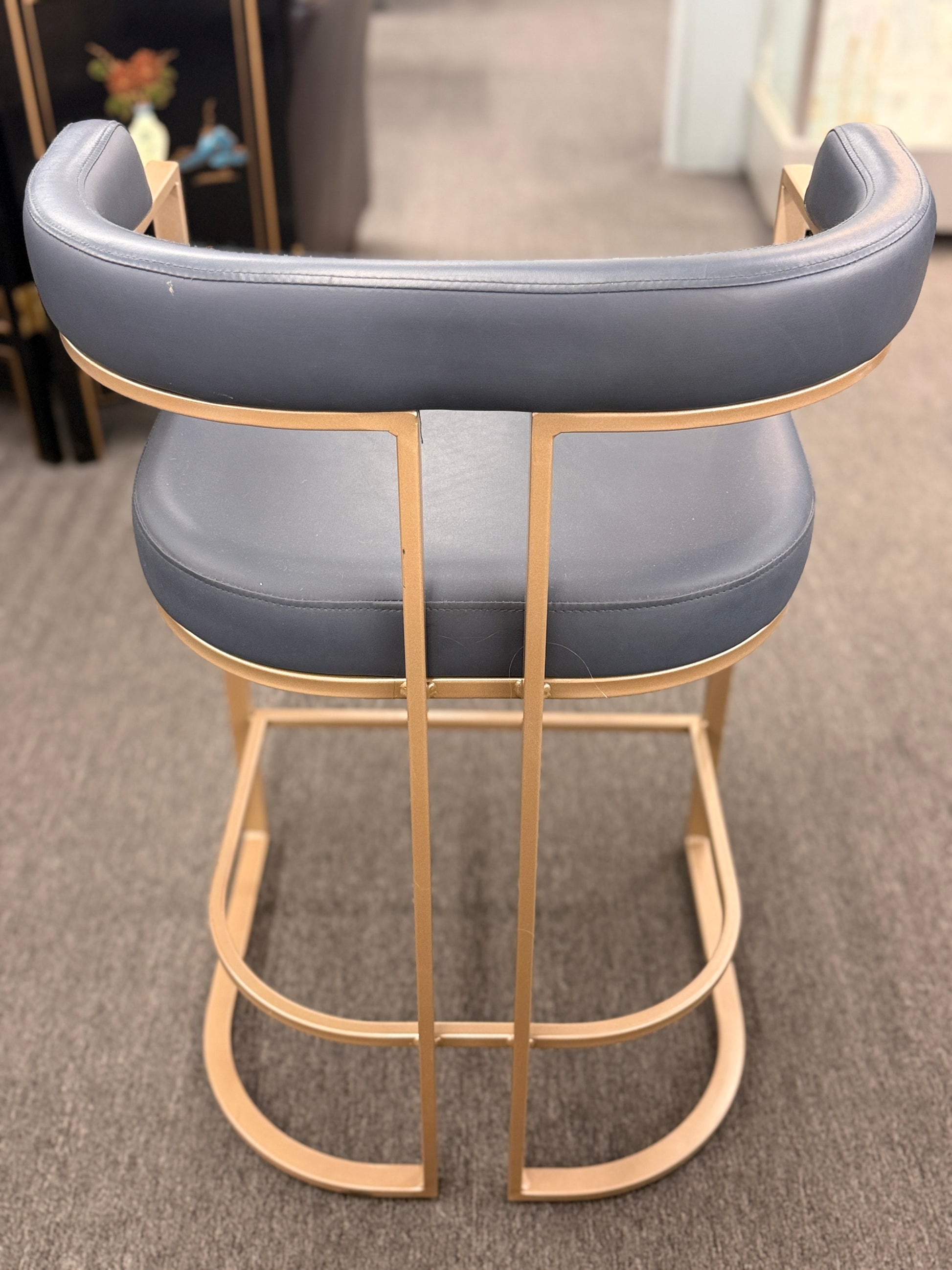 Gray cushioned bar stool with gold metal frame on a carpeted floor.