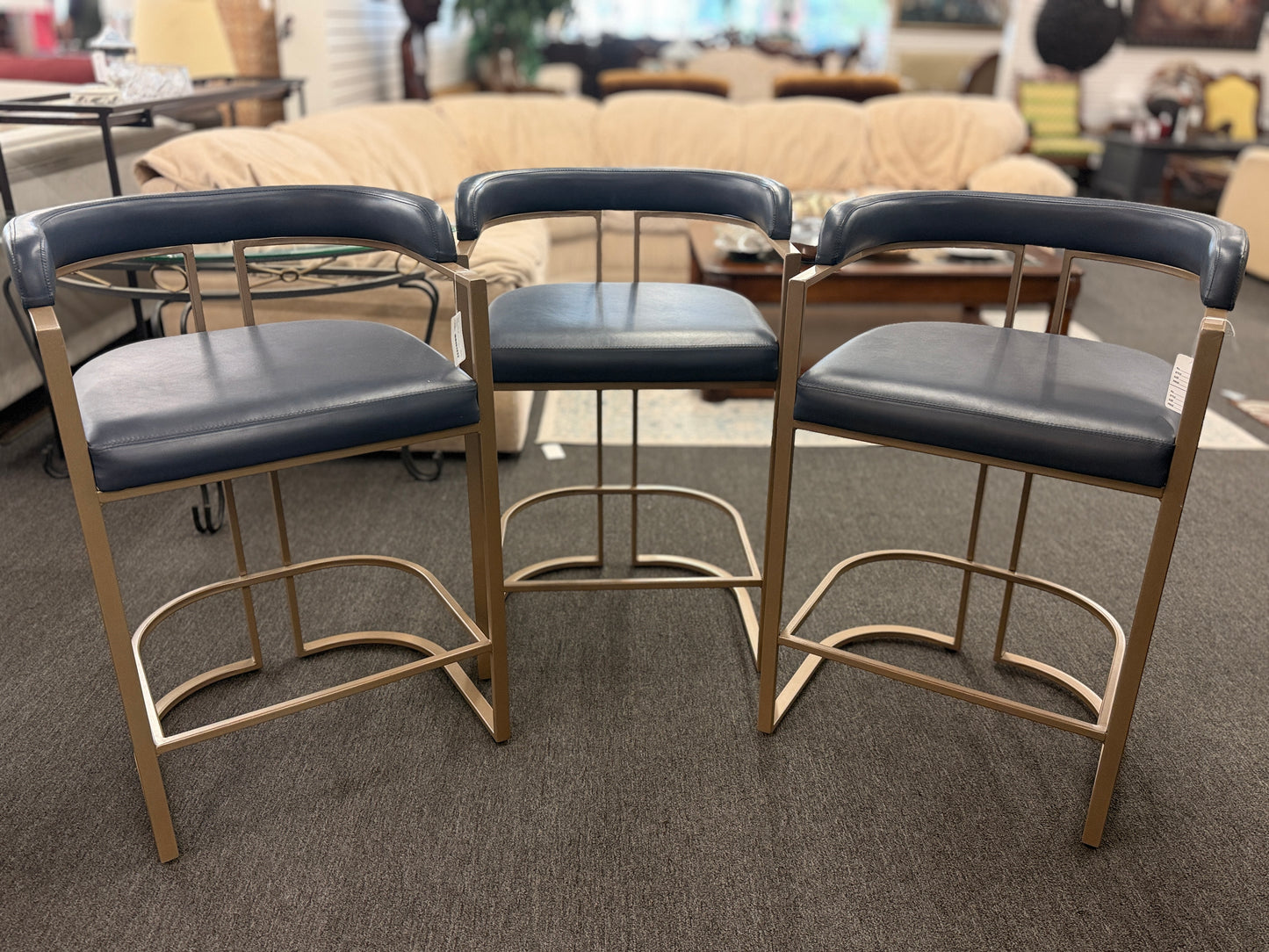 Three bar stools with black seats and gold frames on a carpeted floor.