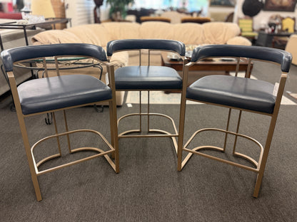 Three bar stools with black seats and gold frames on a carpeted floor.