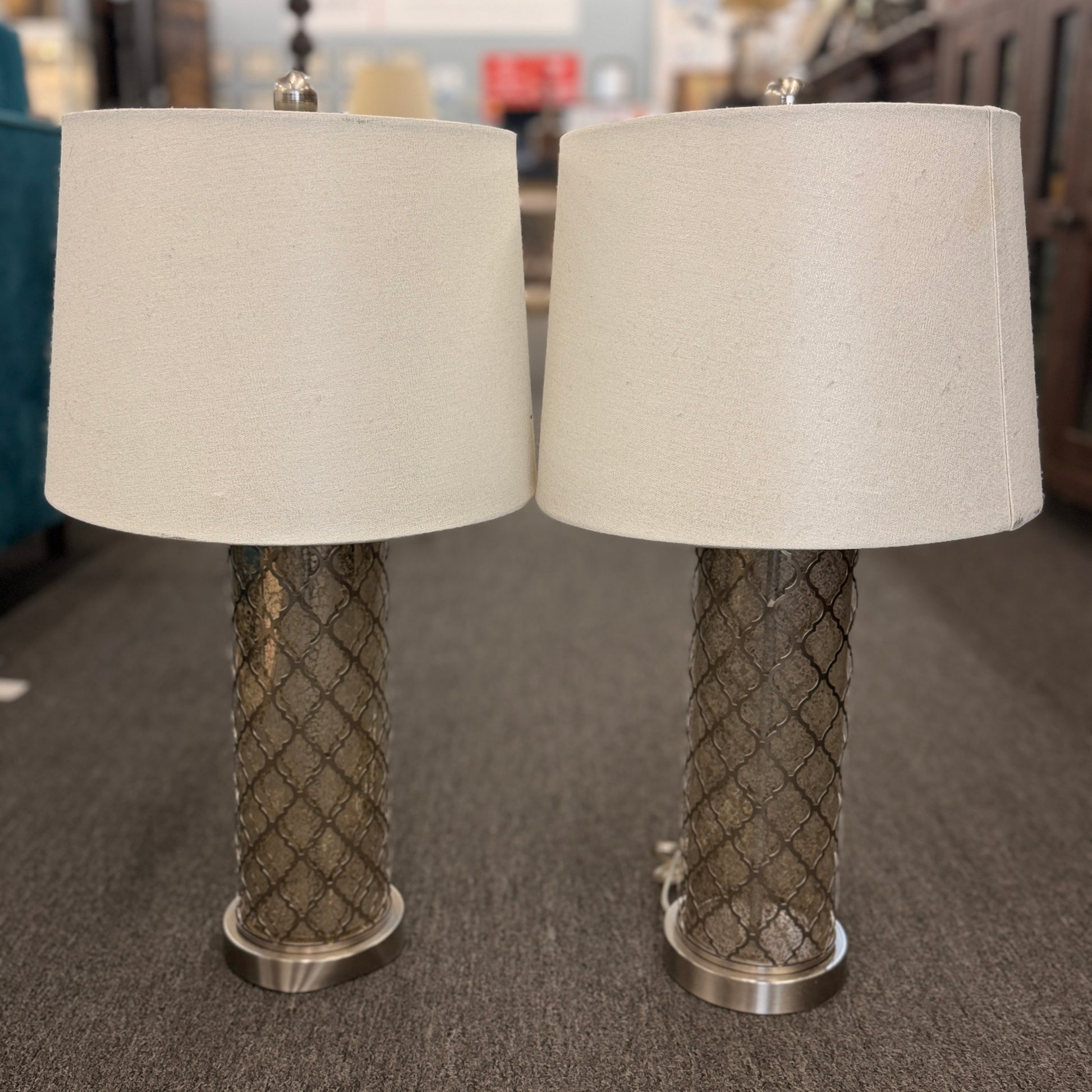 Two table lamps with textured metal bases and beige lampshades on a carpeted floor.